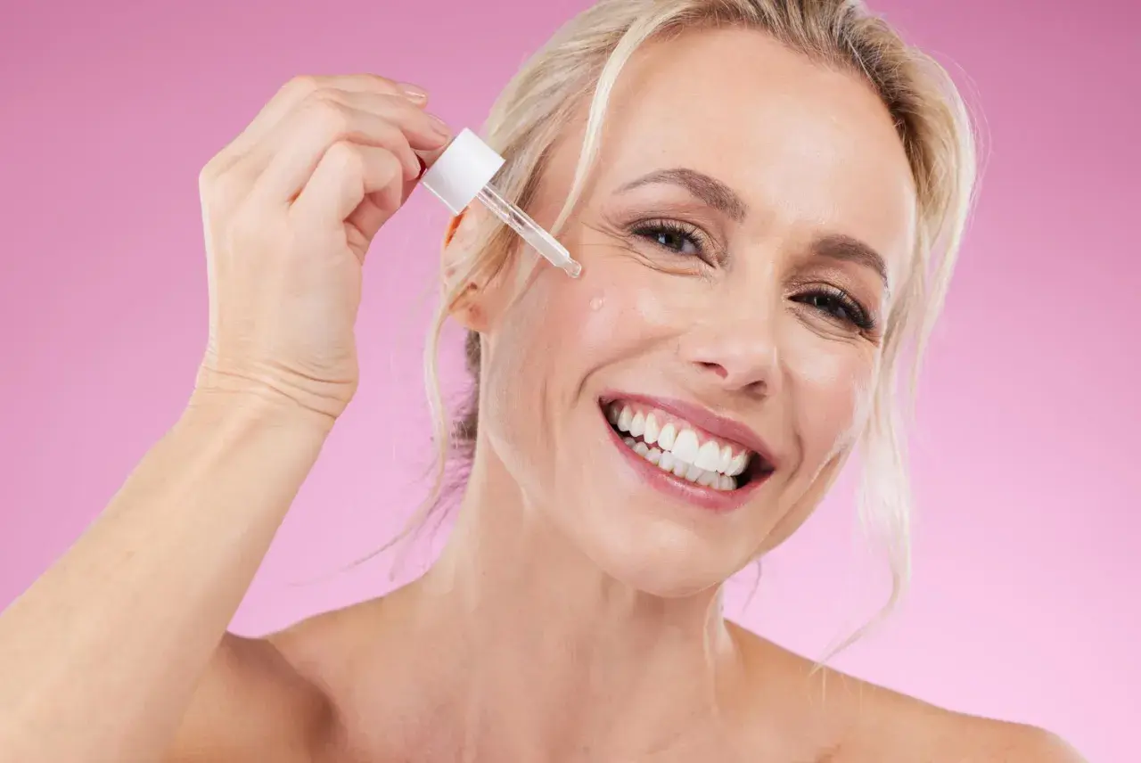 Glad kvinna applicerar serum, oroar sig inte för niacinamide biverkningar.
