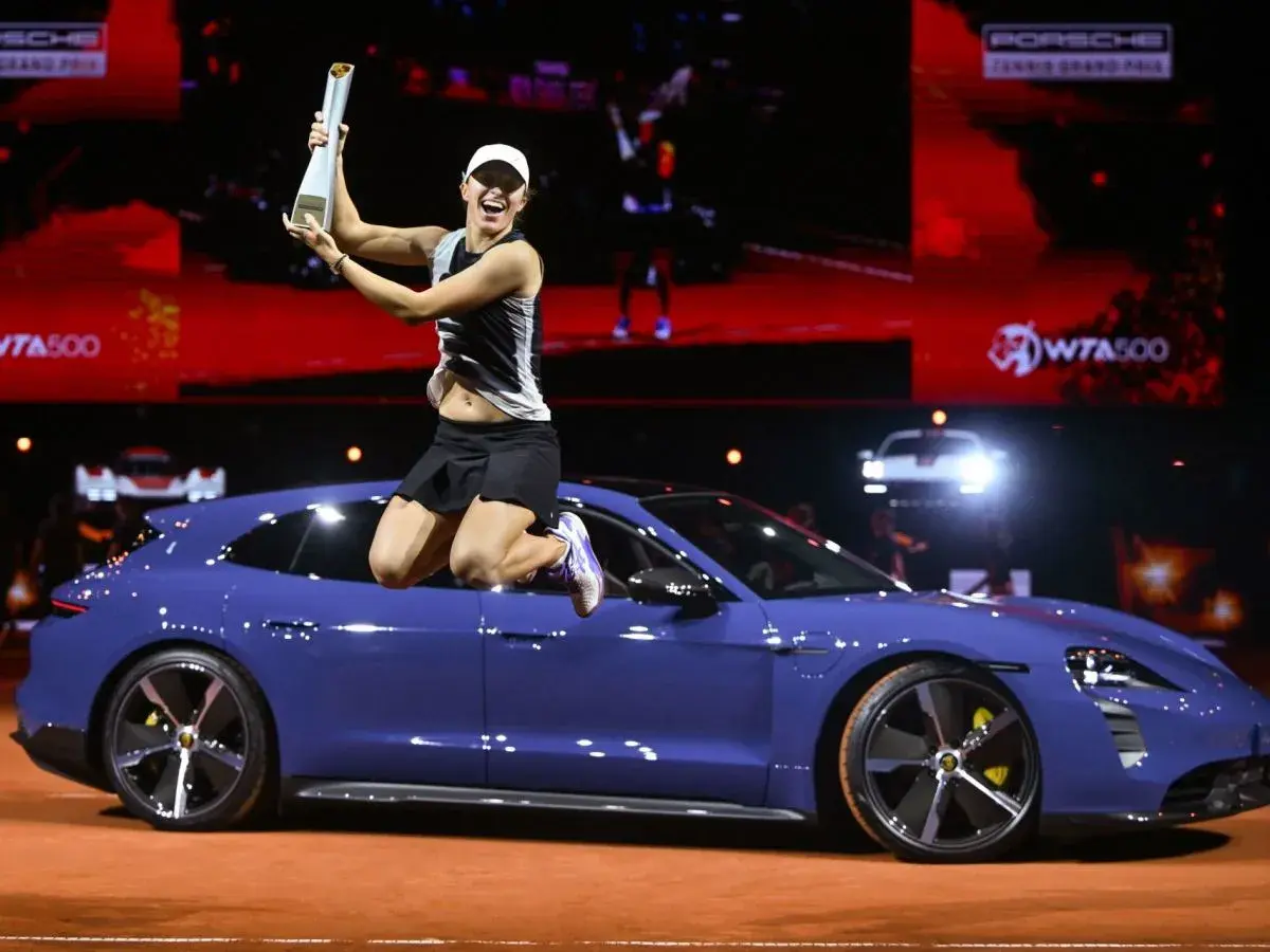 Iga Świątek skacze z pucharem na dachu niebieskiego Porsche, świętując zwycięstwo.