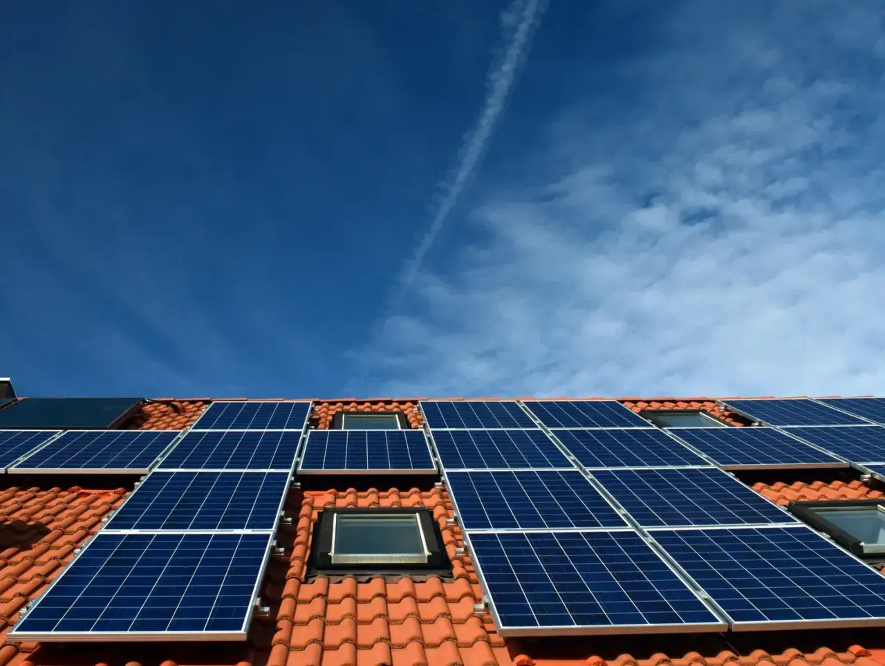 Nowoczesna instalacja PV na dachu z dachówką, pod błękitnym niebem. Panele słoneczne zbierają energię.