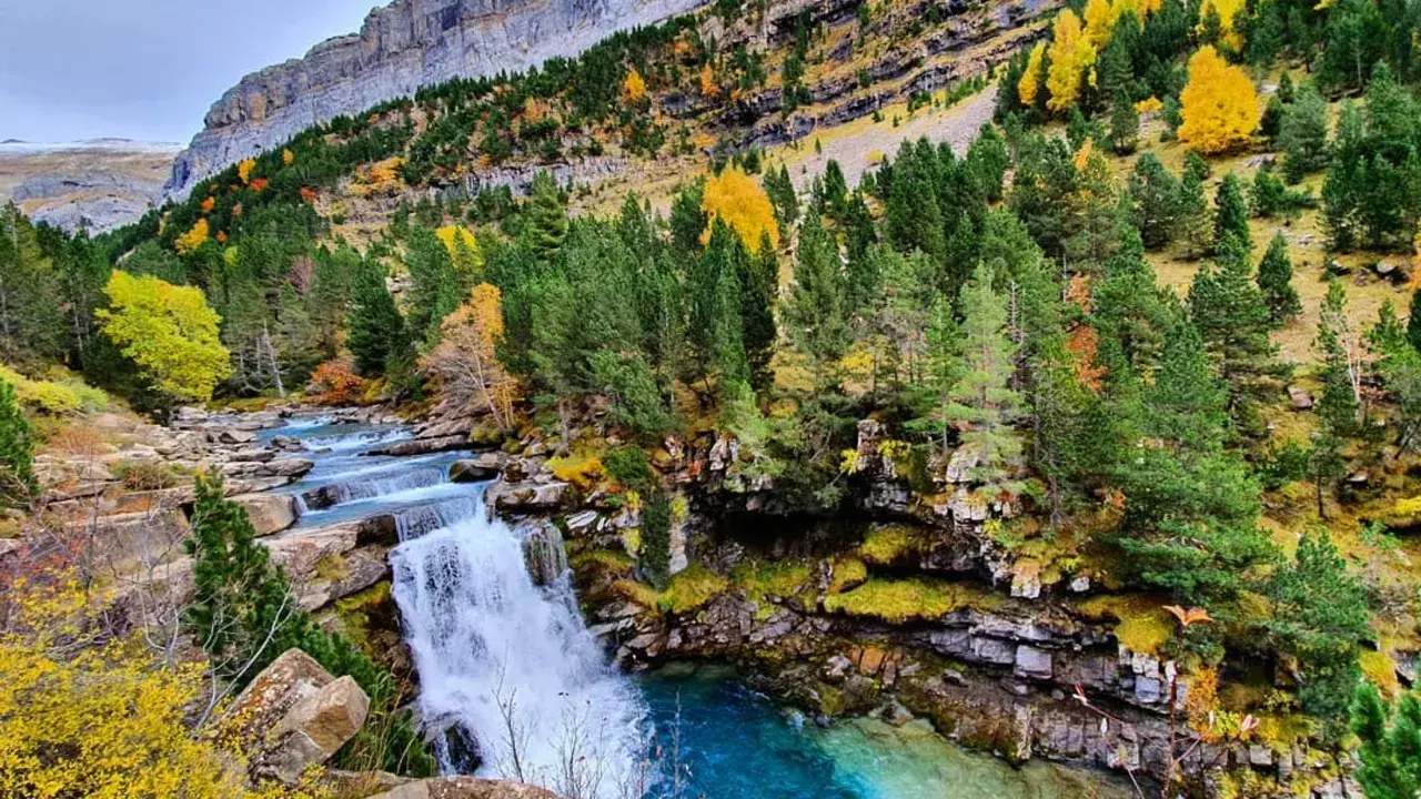 Cascada y río en la ruta Cola de Caballo, rodeados de bosques otoñales y montañas imponentes.