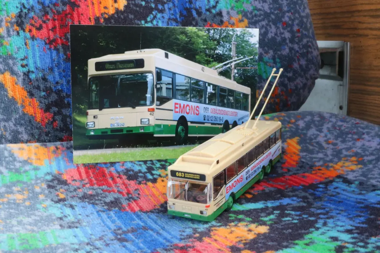 Ein Modell eines Obusses steht neben einer Fotografie eines echten Obusses. Beide zeigen die Aufschrift "EMONS DER GEBÄUDEDIENSTLEISTER".