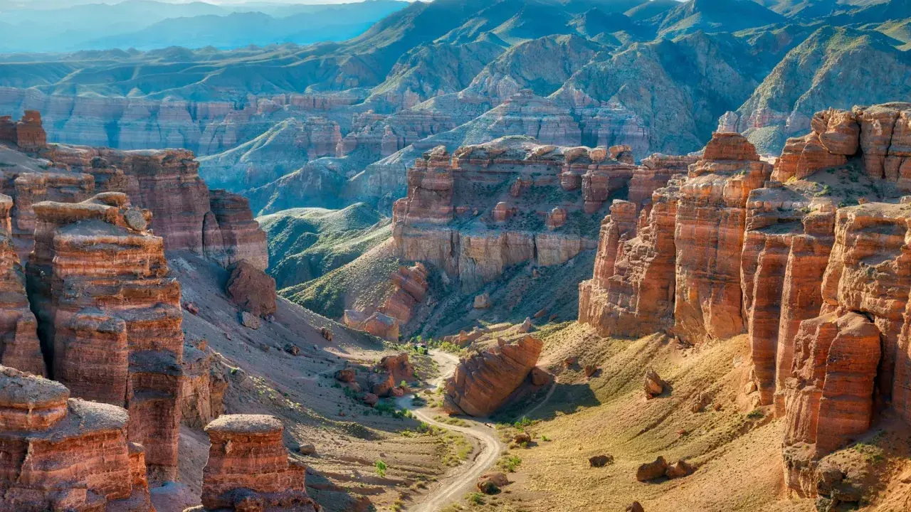 Beeindruckende Schluchten und Berge prägen die Kasachstan Landschaft. Ein gewundener Weg führt durch das Tal, umgeben von roten Felsformationen und grünen Hängen.