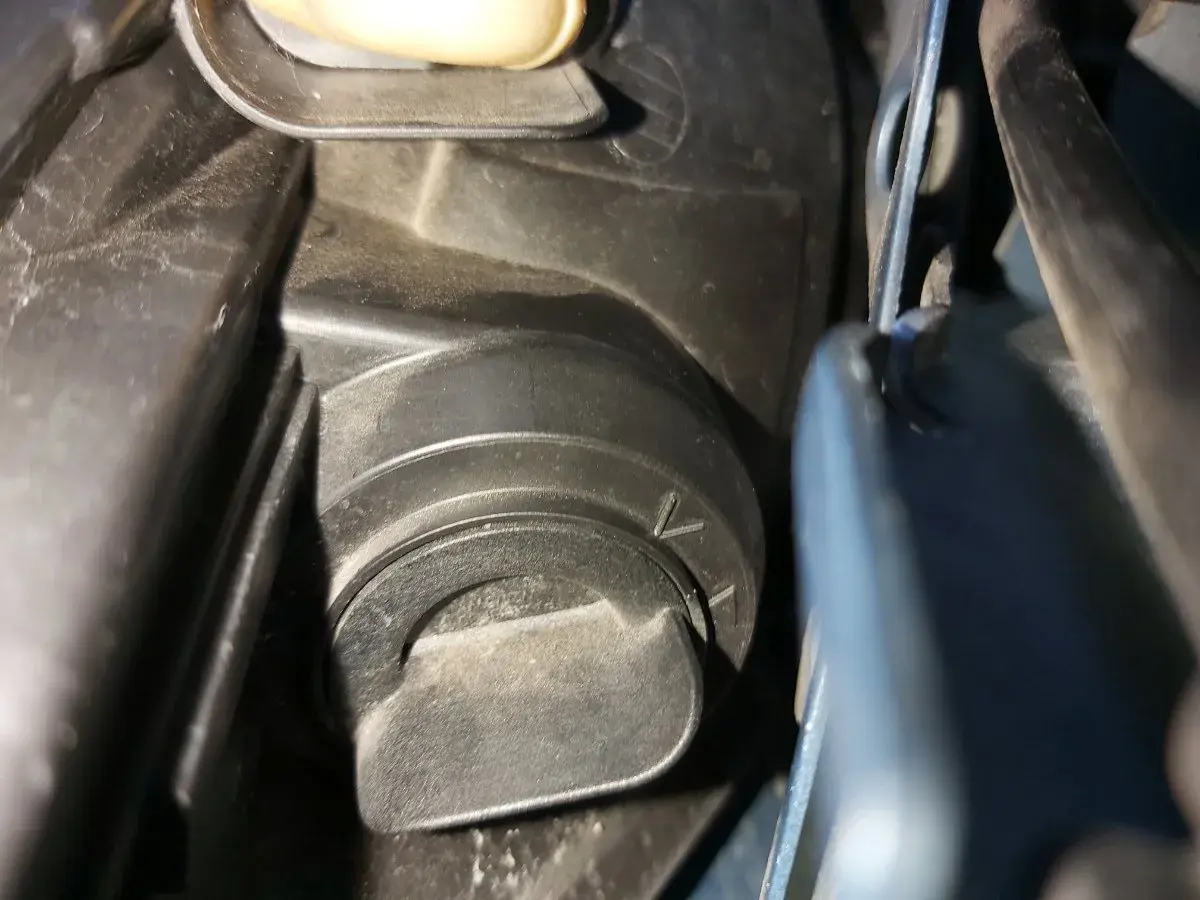 Opel Meriva B wymiana żarówki mijania. Widoczny element mocowania osłony reflektora, przygotowanie do wymiany.
