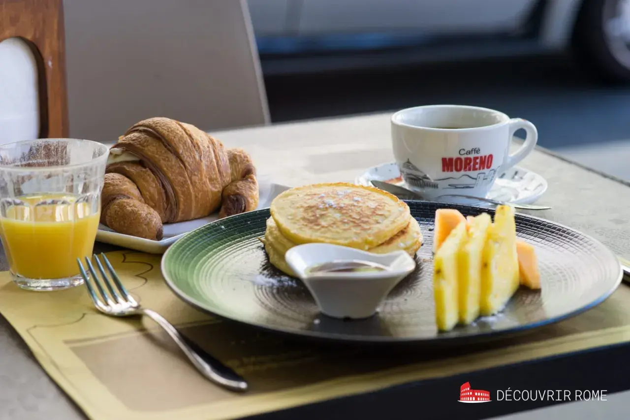 Un délicieux petit déjeuner italien : croissant, pancakes, fruits frais et café. Un régal pour bien commencer la journée !