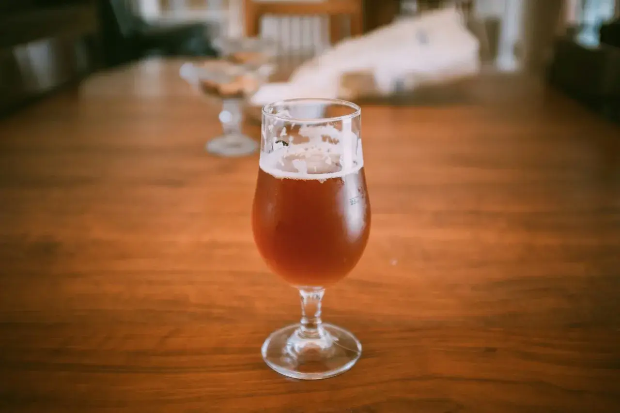 Un bicchiere di birra ambrata su un tavolo di legno. La domanda "quante birre si possono bere al giorno" aleggia nell'aria.