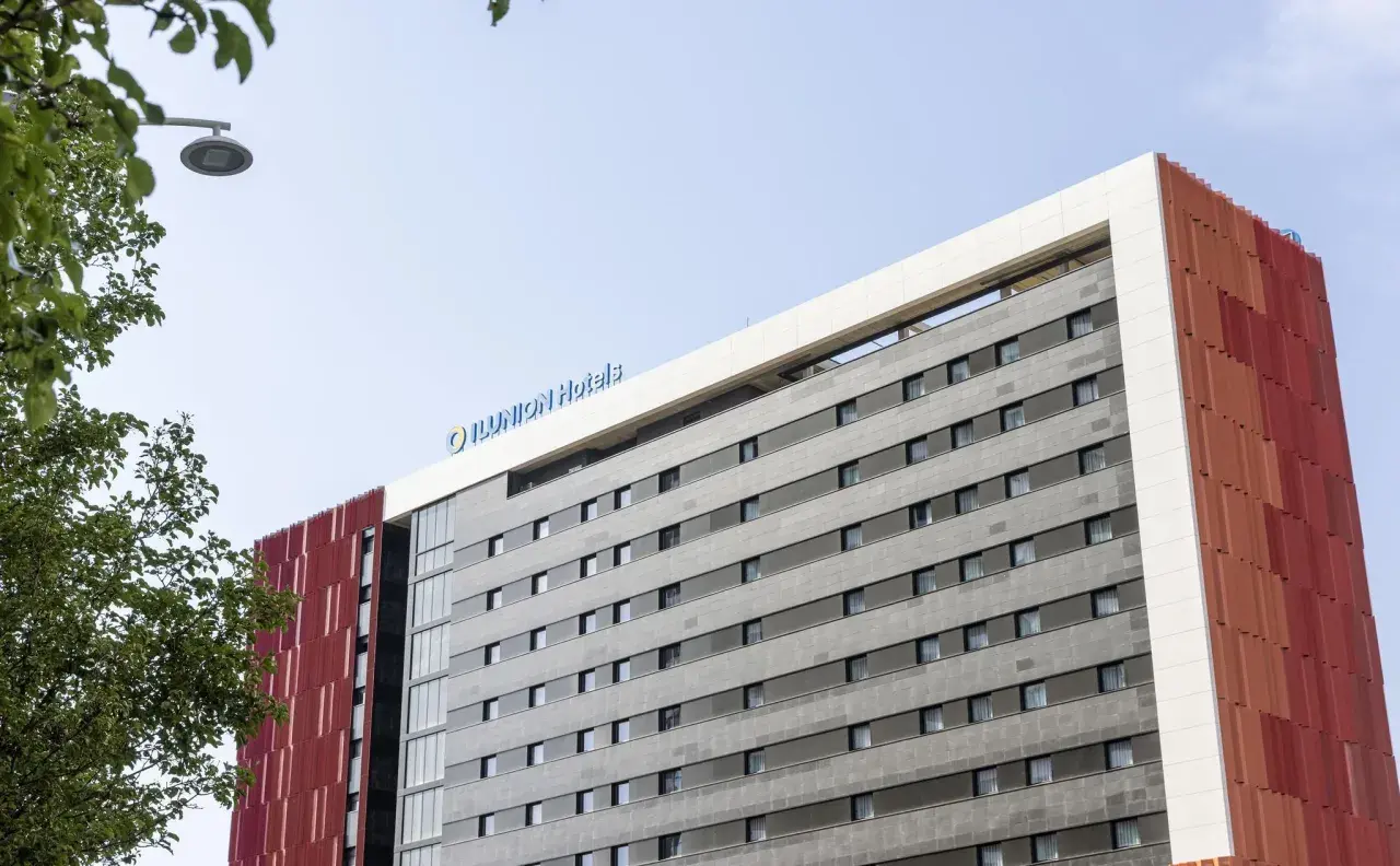 Edificio moderno con el logo "ILUNION Hotels" en la parte superior. Fachada gris con ventanas y detalles rojos.