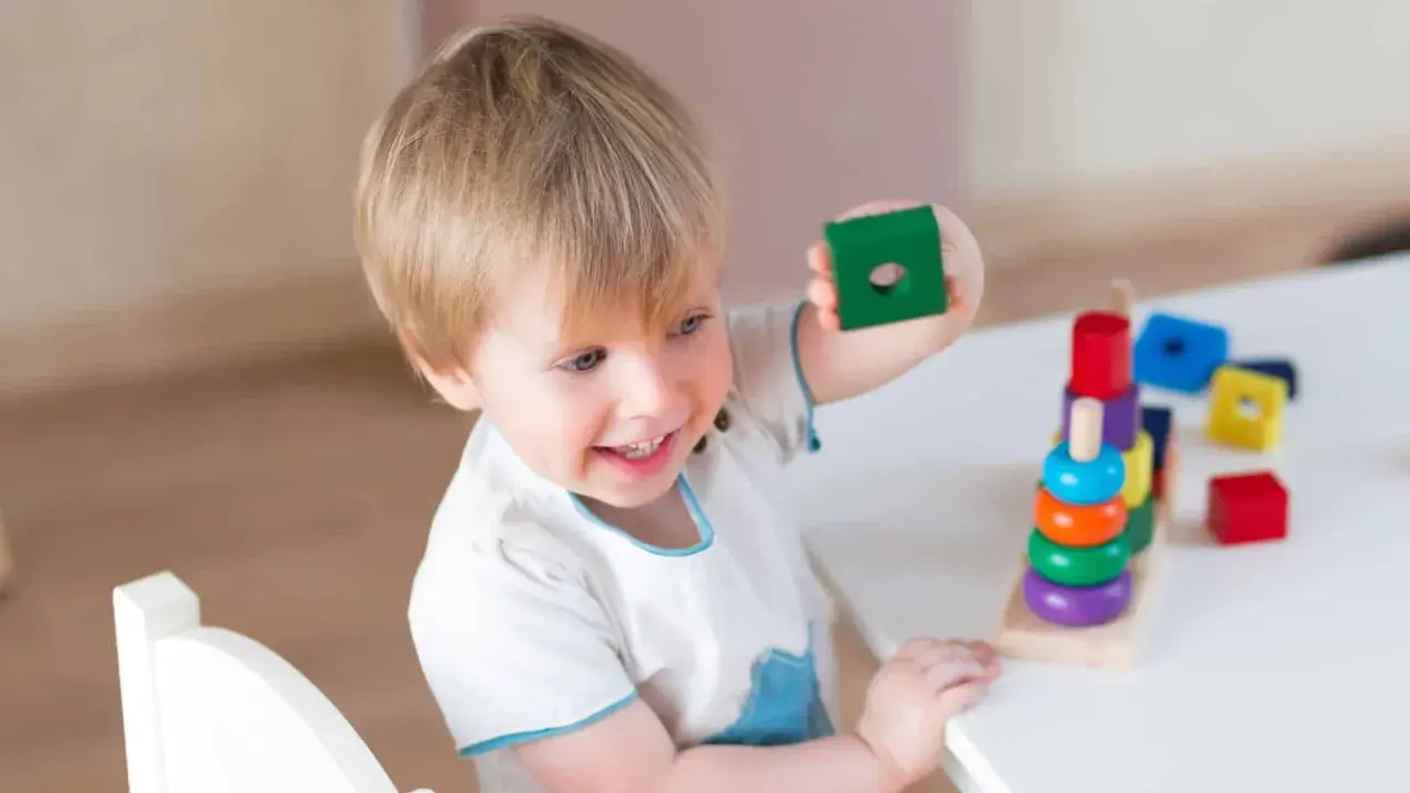Bambino 3 anni sorridente gioca con blocchi colorati impilati.
