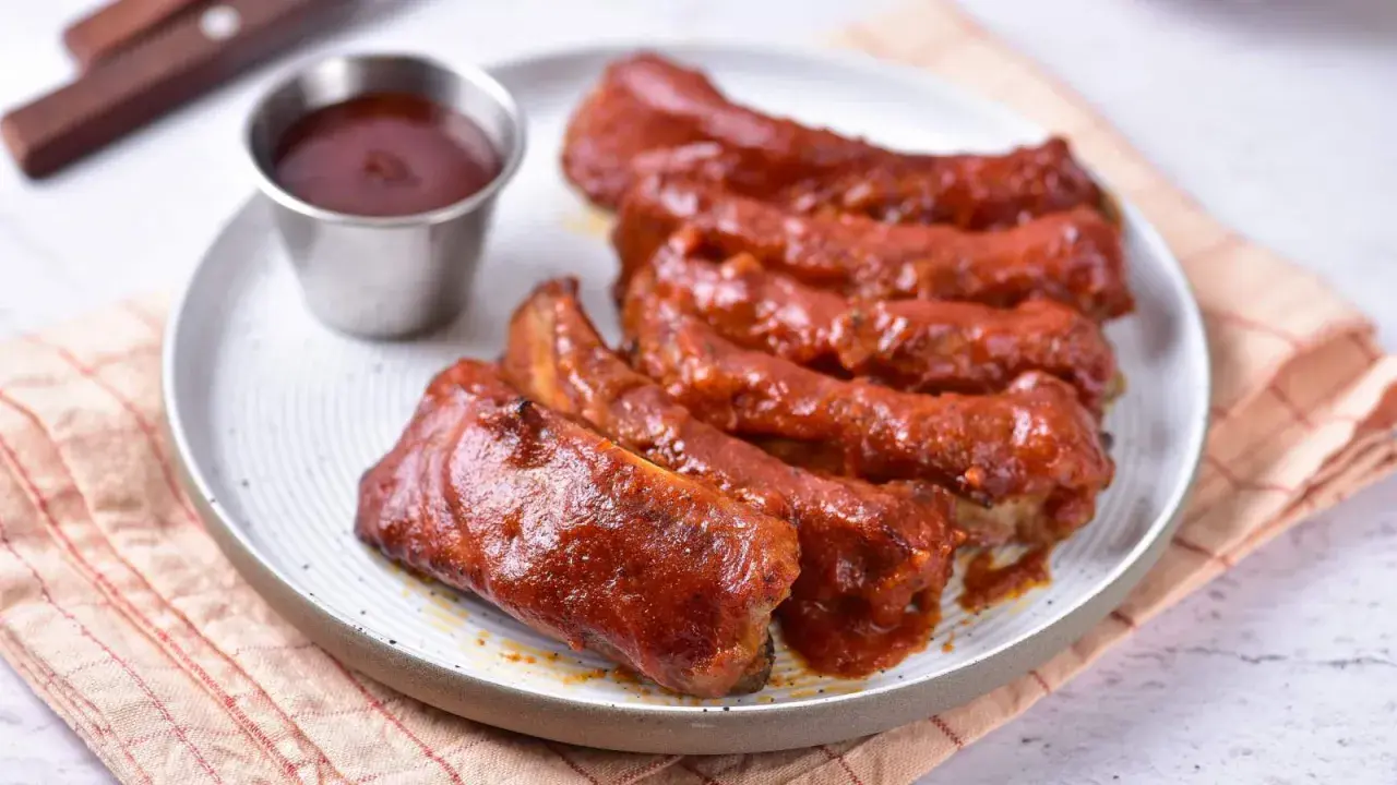 Soczyste żeberka w sosie BBQ, podane na talerzu z małą miseczką sosu. Idealne na letniego grilla.