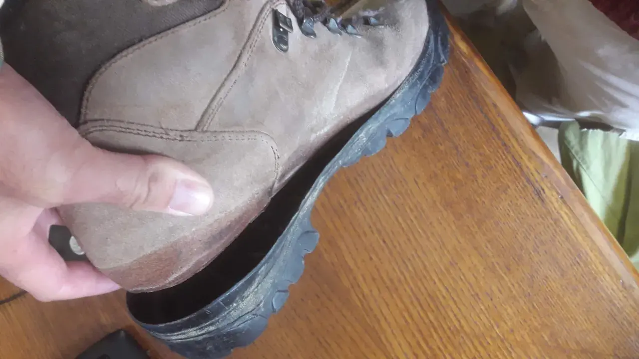 A hand holds a hiking boot where the sole is peeling off, revealing the inside of the shoe.
