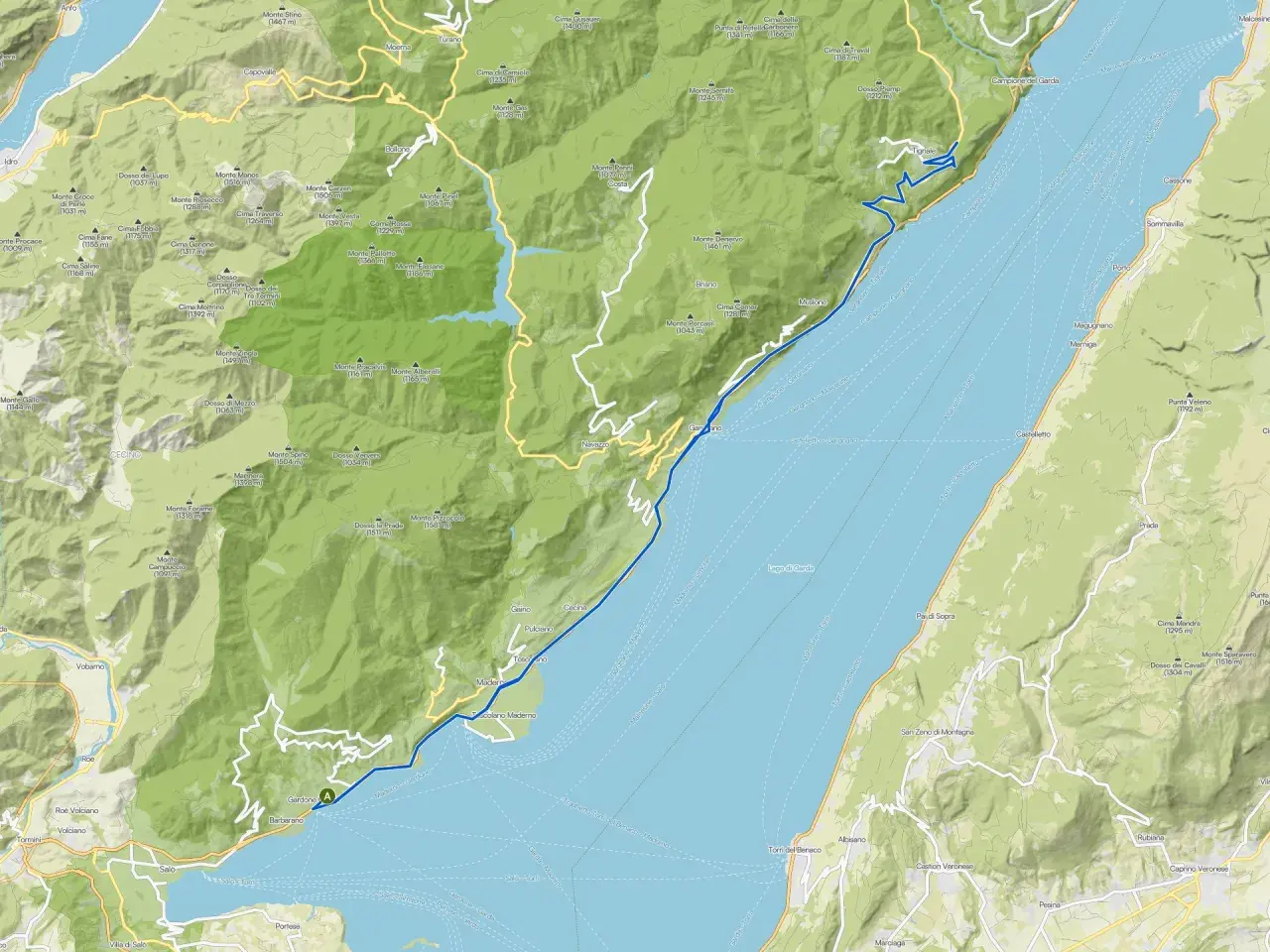 Il lungolago di Gardone Riviera si estende lungo il Lago di Garda, con montagne verdi che si affacciano sull'acqua.