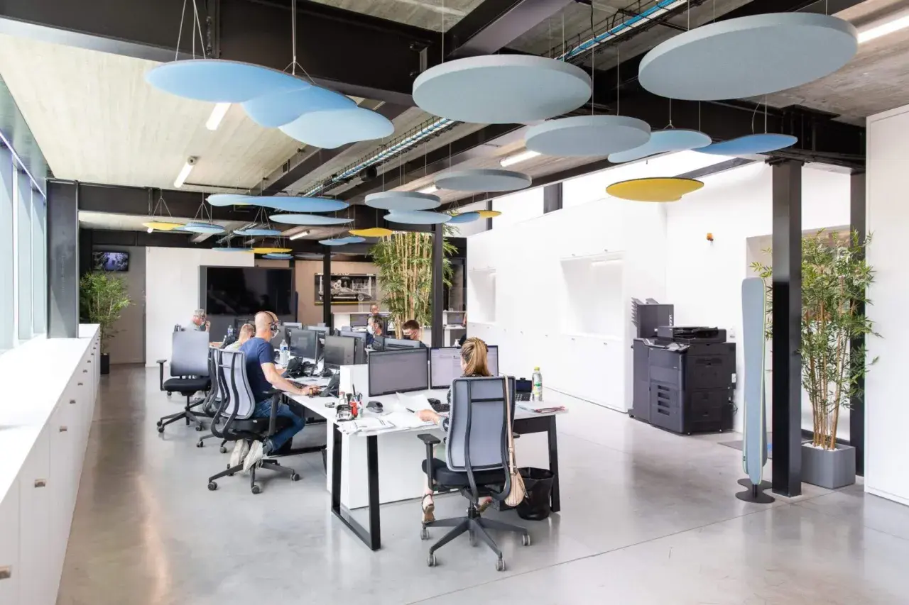 Bureau moderne avec employés concentrés, malgré le bruit ambiant. Des panneaux acoustiques colorés au plafond réduisent le bruit au travail.