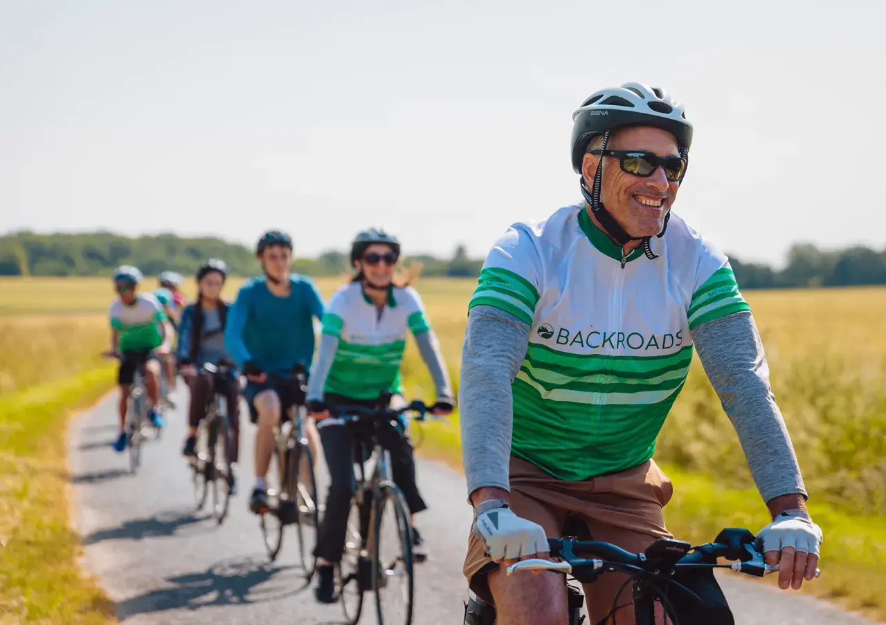 A group enjoys family cycling holidays on a sunny day, riding bikes down a paved path through golden fields.
