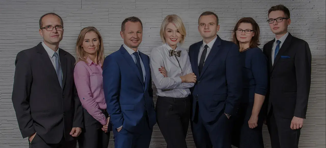 Grupa prawników w eleganckich strojach pozuje do zdjęcia na tle ściany z cegły.