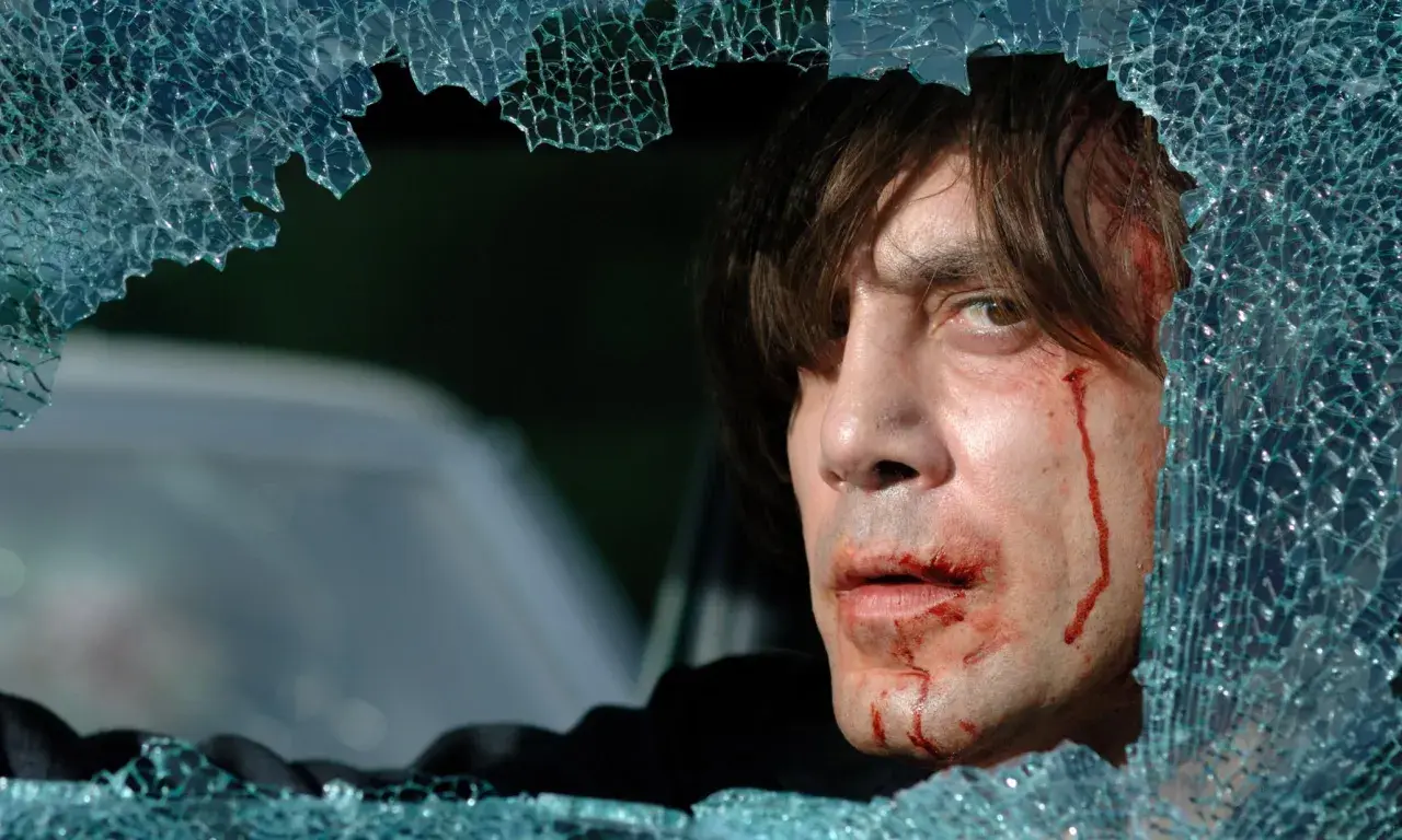 Javier Bardem w jednym z mrocznych filmów, z krwawiącą twarzą, patrzy przez pękniętą szybę.