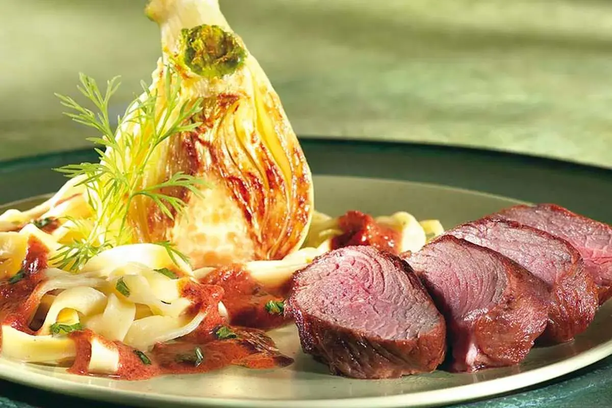 Tranches de rumsteak d'agneau rosé, accompagnées de pâtes fraîches, d'une sauce rouge et d'un fenouil braisé.