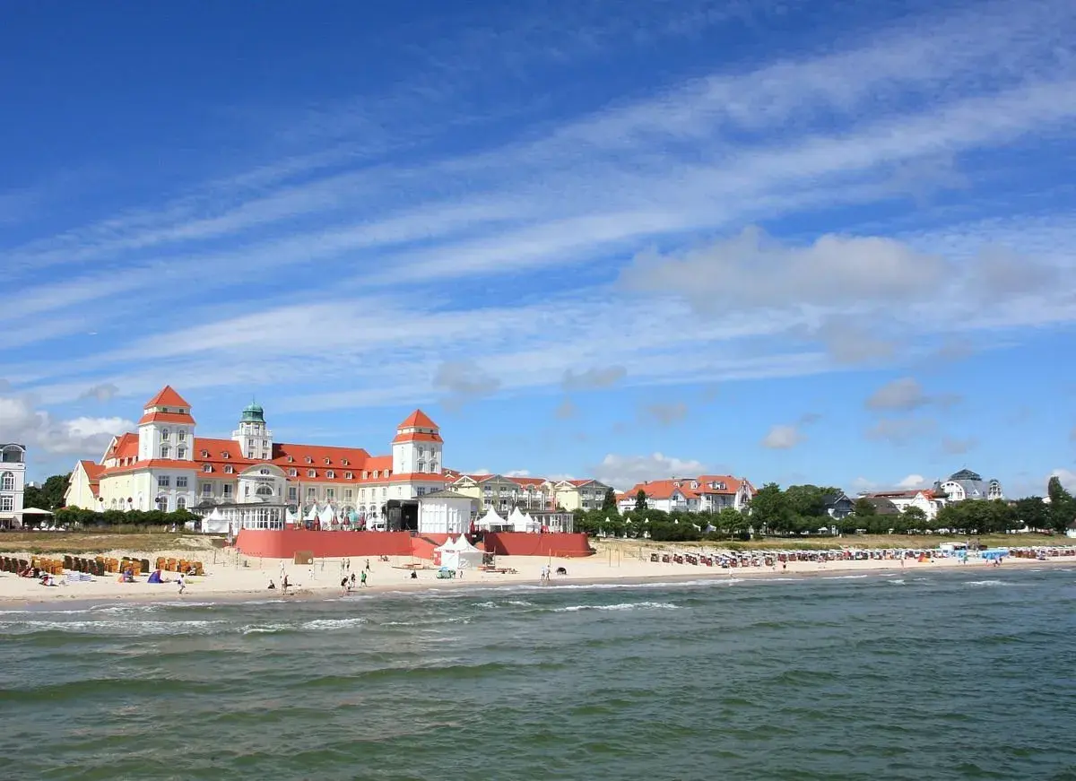 Prachtvolles Gebäude am Strand des Ostseebad Binz, mit roten Dächern und Türmen, unter blauem Himmel mit Wolken.
