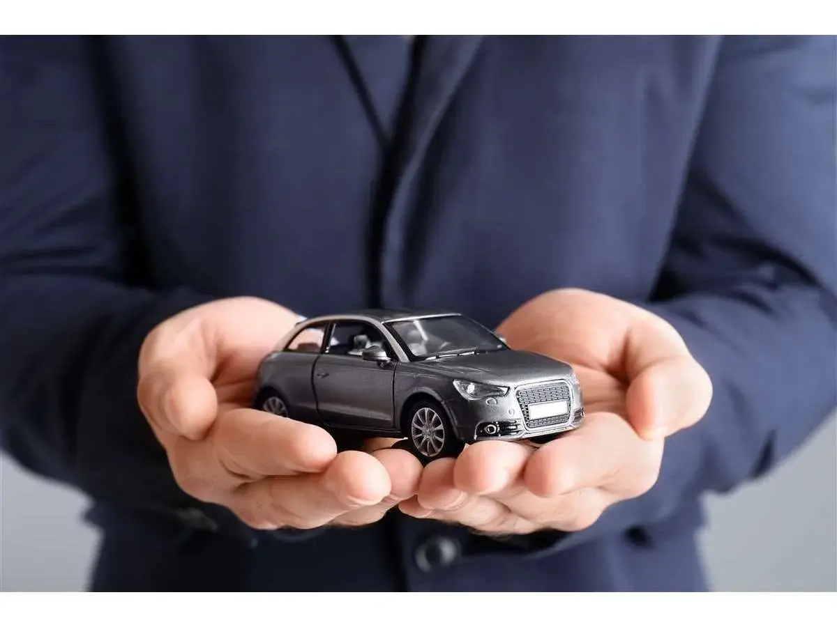 Mani che sorreggono un modellino d'auto grigio. Non dimenticare la tua assicurazione scaduta 15 giorni fa!