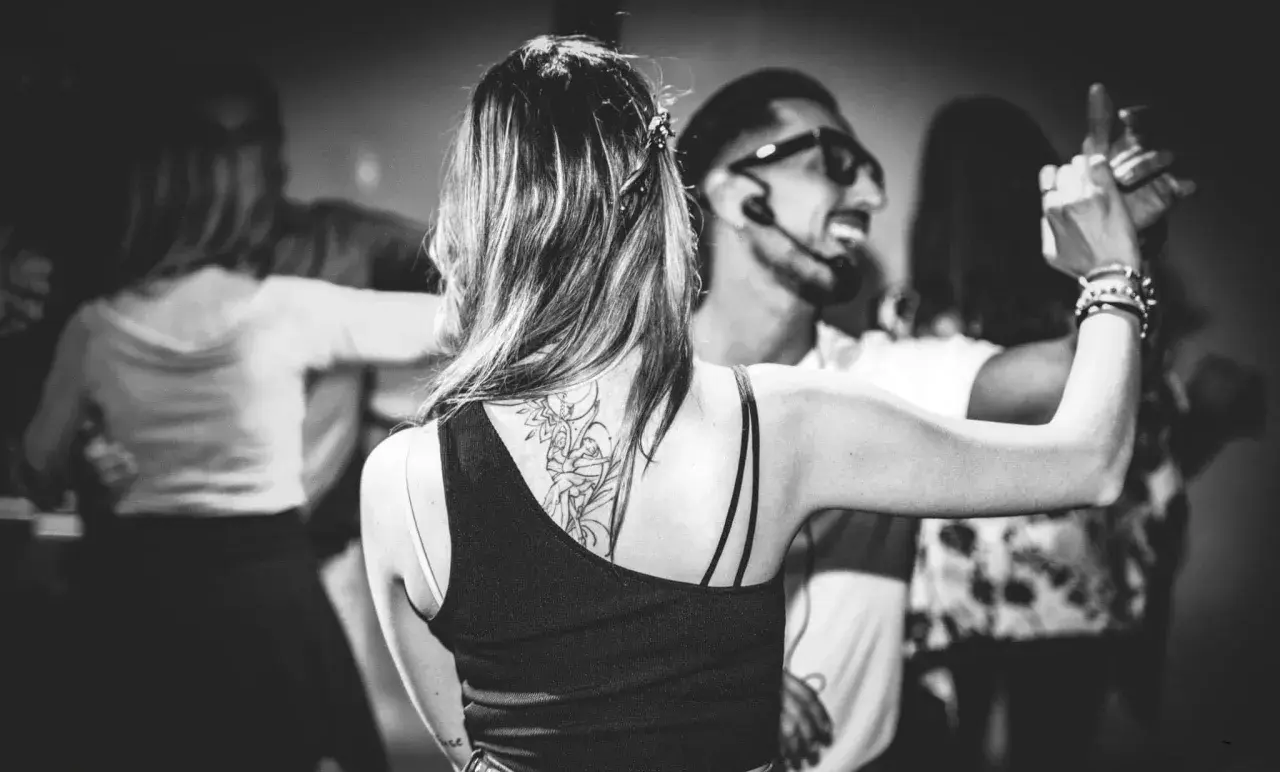 Coppie danzano in un corso di ballo latino americano. La donna in primo piano ha un tatuaggio sulla schiena.