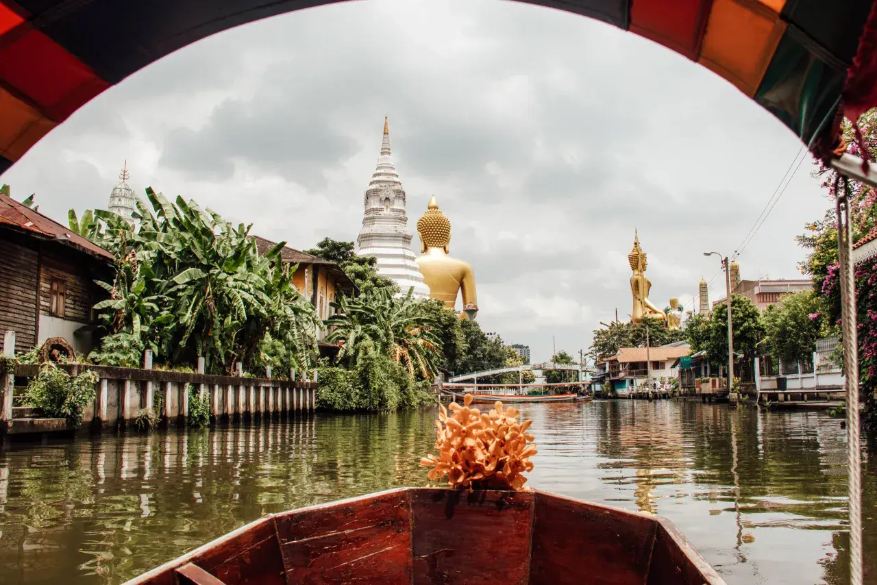 Bootsfahrt auf einem Kanal in Bangkok mit Blick auf goldene Buddha-Statuen und Tempel. Entdecken Sie diese Bangkok Geheimtipps abseits der ausgetretenen Pfade.