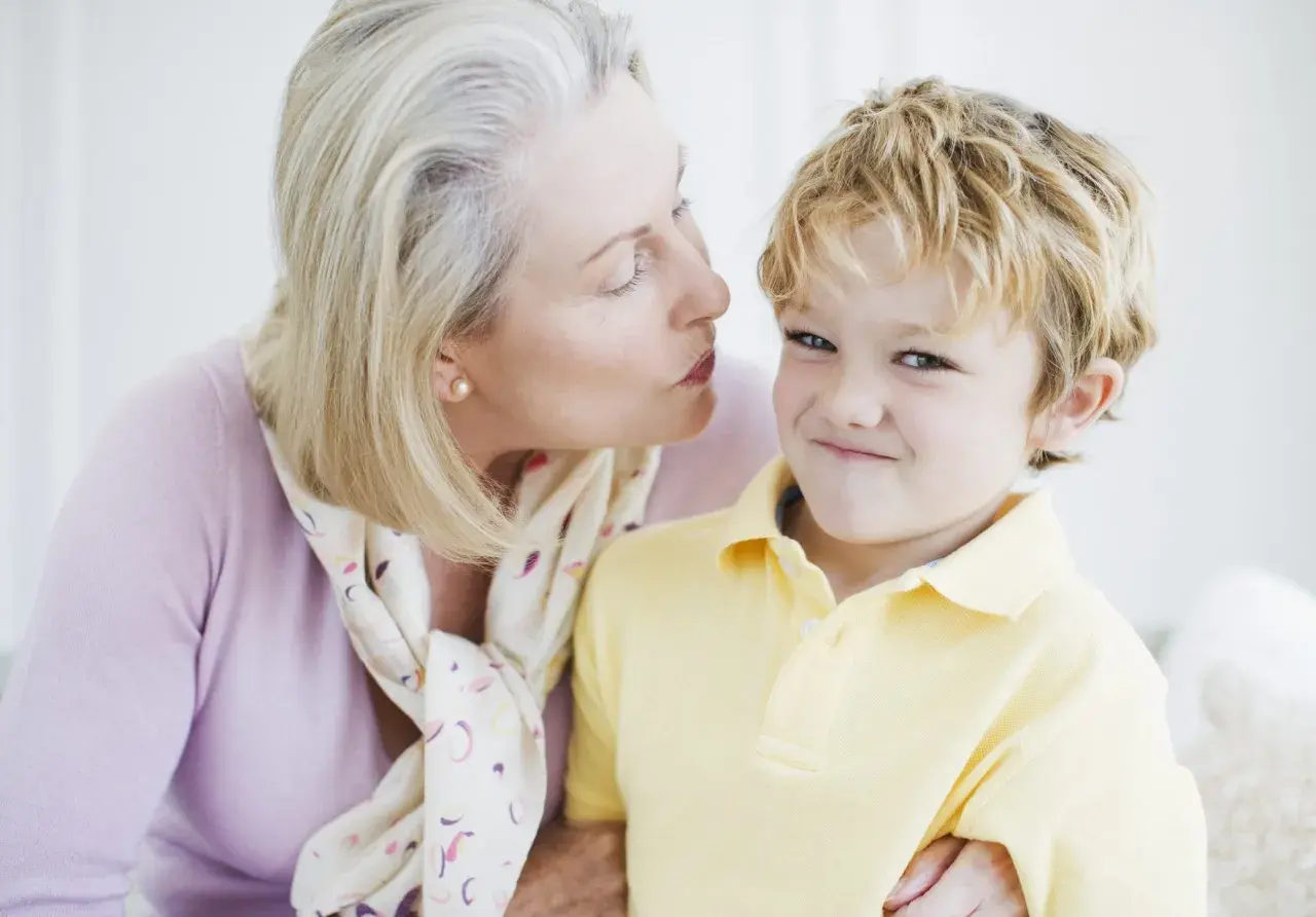 Una nonna bacia un bambino sorridente. Nonostante la tenerezza, i bambini non si baciano sempre, ma questo momento è speciale.