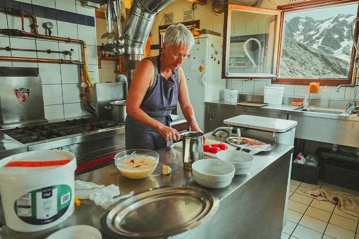 Une femme prépare des ingrédients dans une cuisine de montagne, un aperçu de son quotidien à travailler dans un refuge.