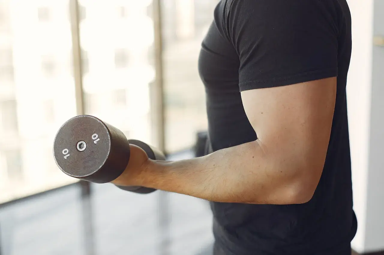 Mężczyzna wykonuje ćwiczenia na biceps z hantlem 10 kg. To jedne z najlepszych ćwiczeń na biceps.