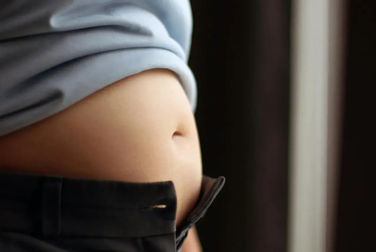En svullen mage, kanske gravid, syns under en ljusblå tröja och över ett par mörka byxor.
