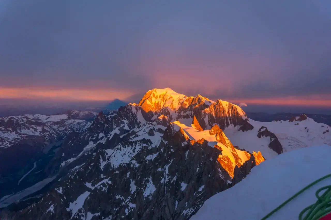 Złote światło wschodu słońca oświetla szczyt Mont Blanc, rzucając długi cień na ośnieżone góry.