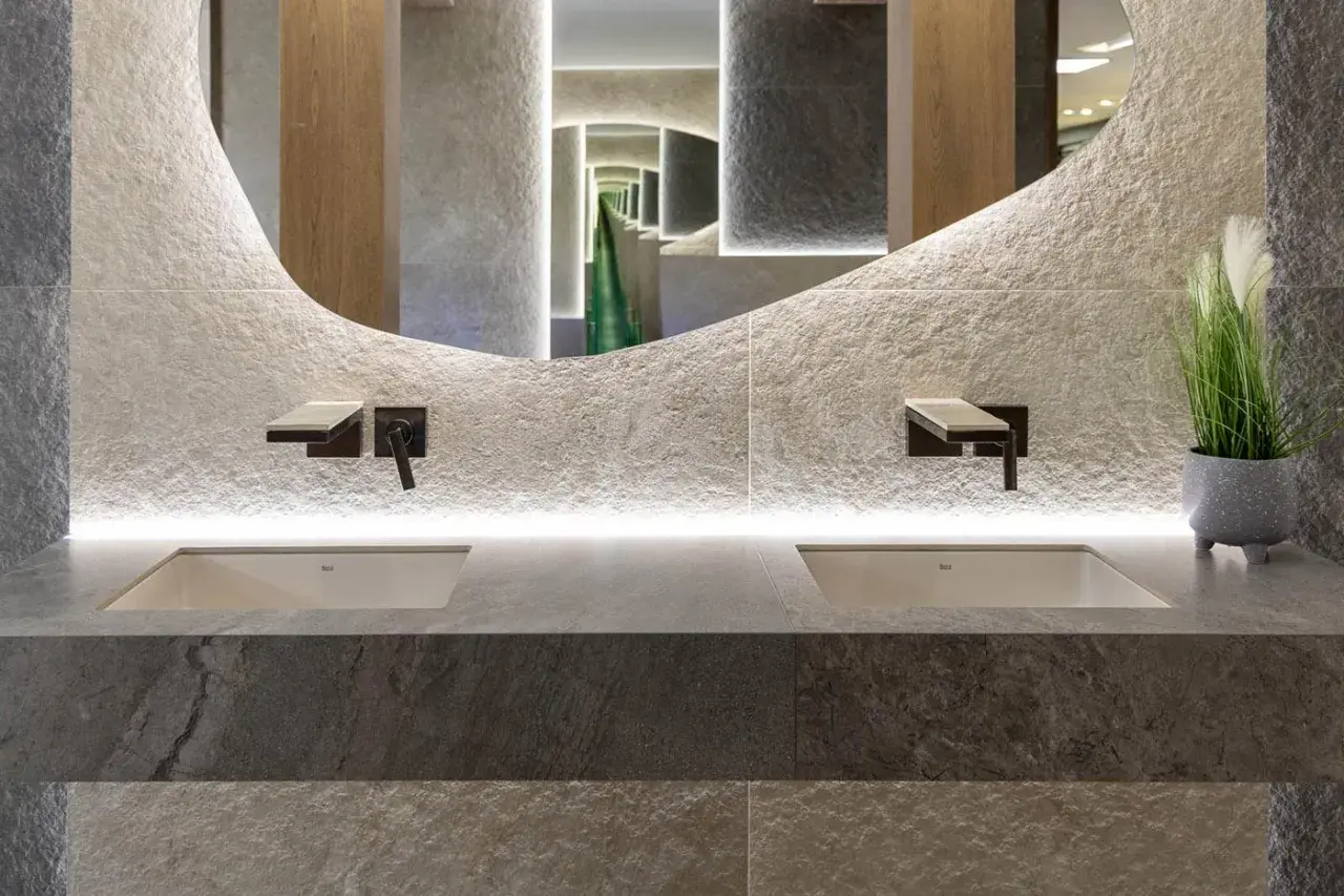 Nowoczesna łazienka z dwoma umywalkami, kamiennymi płytkami i rośliną, idealnie oddająca zasady biophilic design.