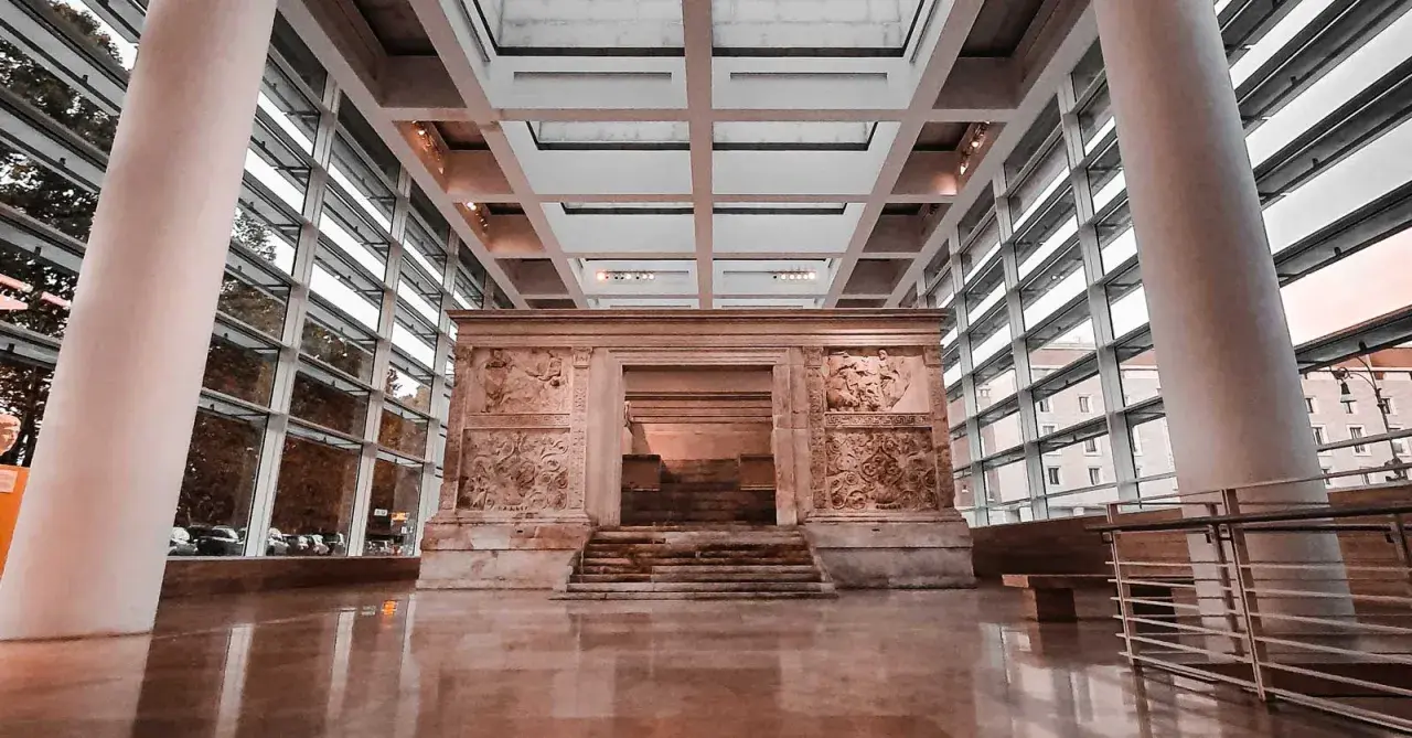 L'Ara Pacis, un altare monumentale con rilievi antichi, si erge maestoso in un moderno spazio espositivo con ampie vetrate.