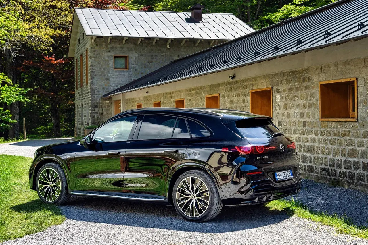 La nuova Mercedes GLC 2026 nera lucida parcheggiata davanti a una casa in pietra con tetto grigio, immersa nel verde.