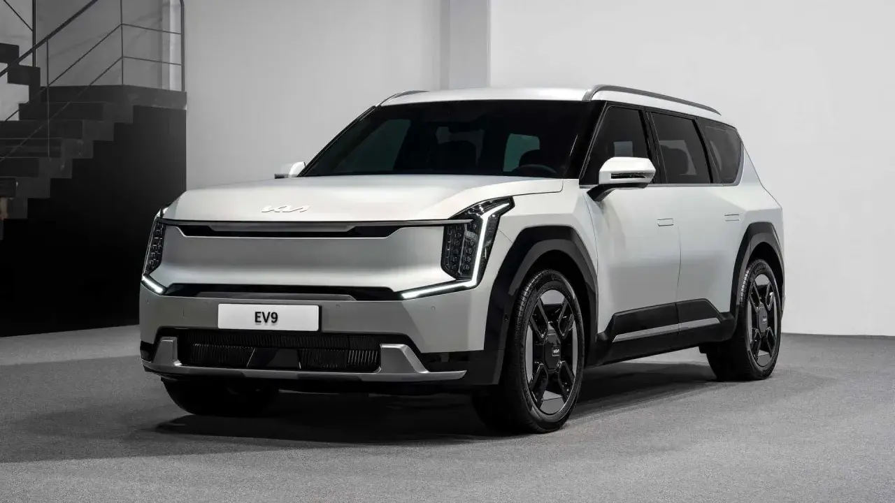 Biały, futurystyczny SUV Kia EV9 z charakterystycznymi światłami LED i masywnymi felgami stoi na szarym tle.