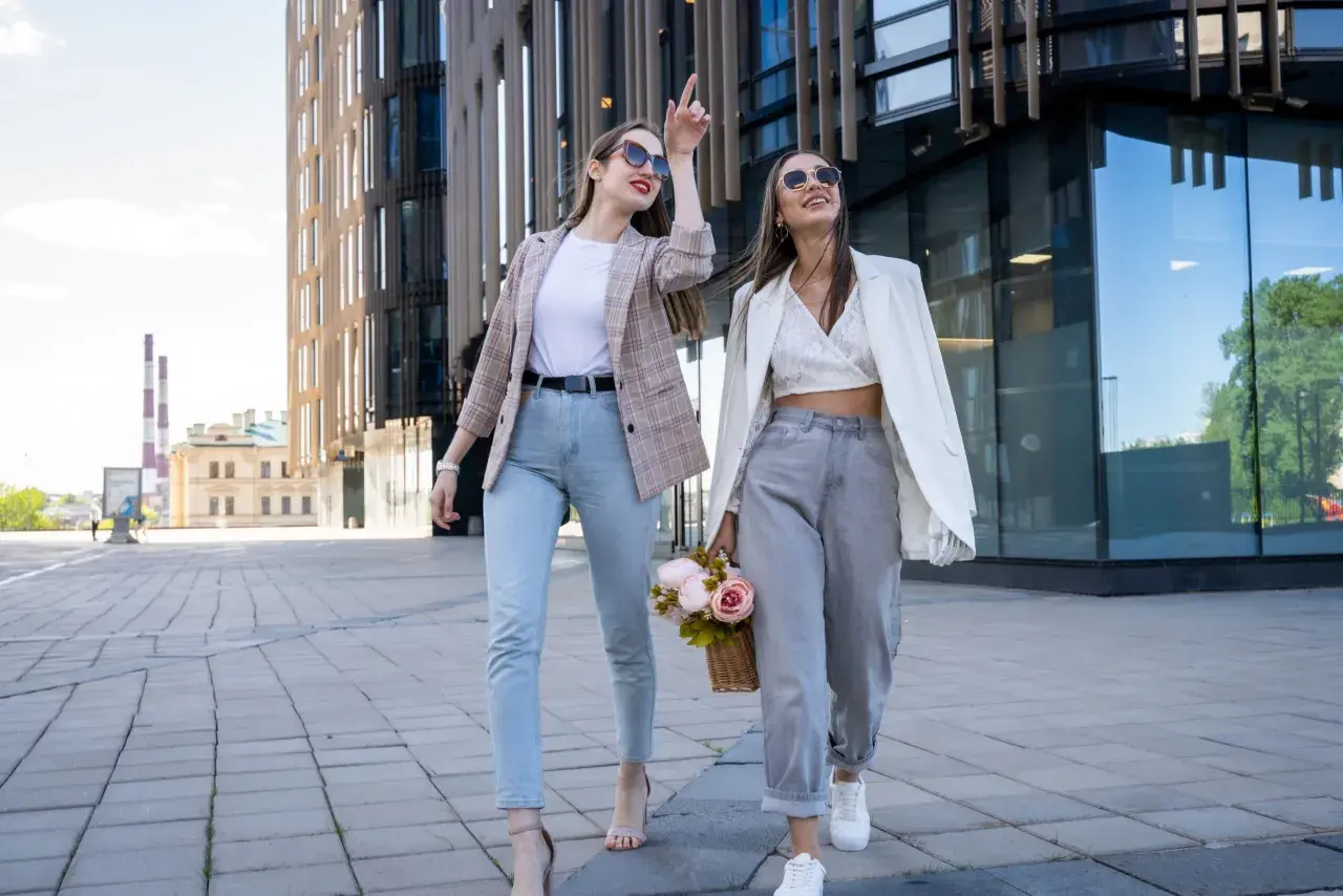 Dwie kobiety w modnych stylizacjach spacerują przed nowoczesnym budynkiem. Ich ubiór sugeruje, że to polskie marki znane na świecie.