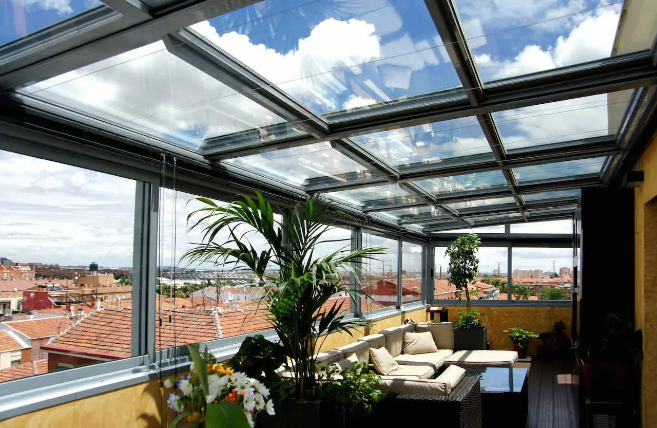Disfruta de vistas panorámicas desde este cerramiento parcial terraza ático. Sofá cómodo, plantas y un cielo azul con nubes.
