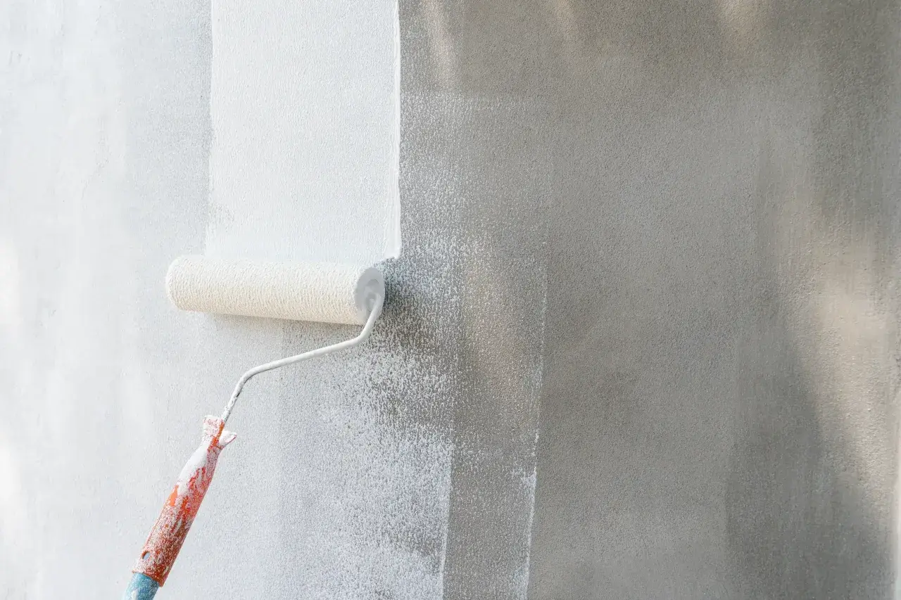 Rodillo aplicando imprimación blanca sobre pared gris. La imprimación prepara la superficie para la pintura.