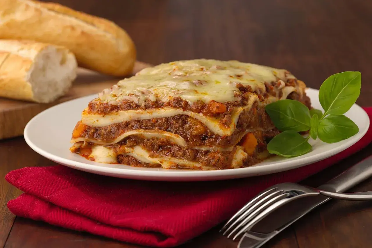 Herzhafte Lasagne mit Hackfleisch und Käse, dazu Baguette. Welcher Wein zu Lasagne passt, ist eine Frage des Geschmacks, aber ein kräftiger Rotwein ist oft ideal.