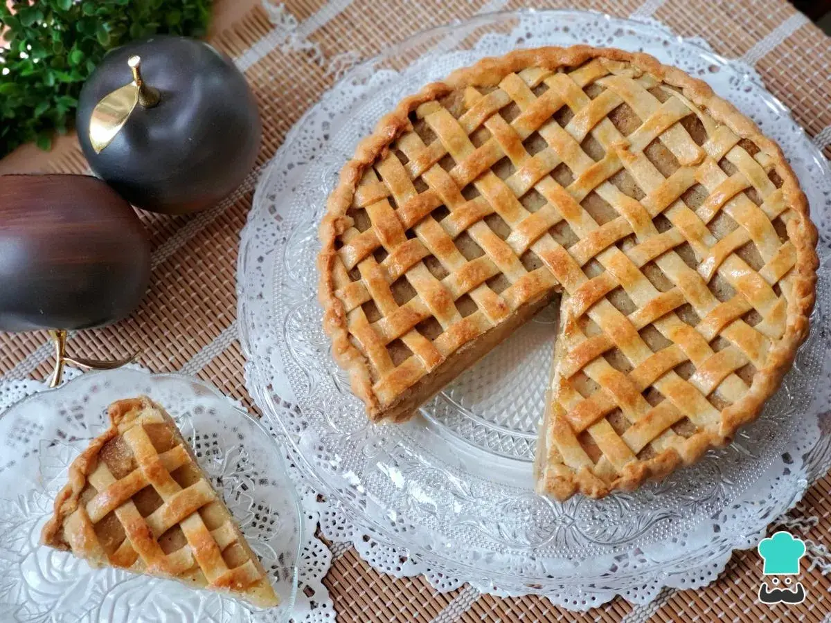 Tarta de manzana de la abuela, dorada y con un enrejado perfecto. Un trozo ya servido en un plato de cristal.