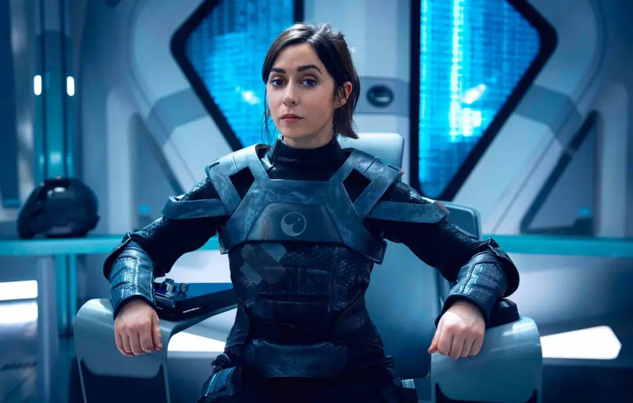 Une femme en armure futuriste, assise dans un cockpit, pourrait être un personnage de Black Mirror saison 7.