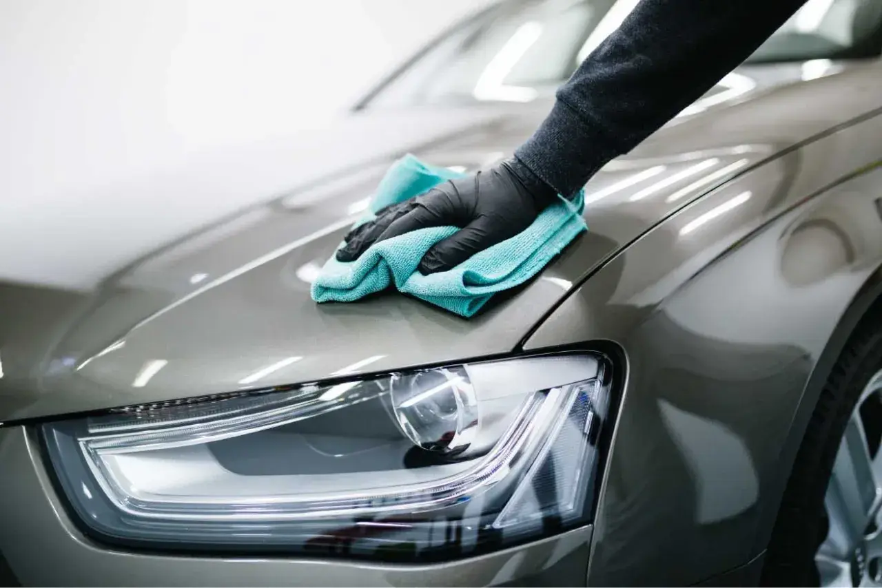 Mano guantata lucida la carrozzeria di un'auto con un panno azzurro. Il dettaglio mostra la cura per il costo lucidatura auto.