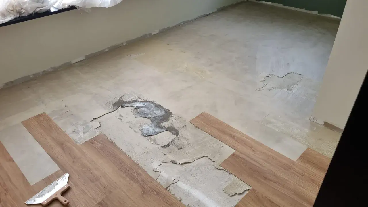 Il pavimento in PVC si solleva in più punti, mostrando il sottofondo danneggiato. Si vedono nuove doghe di legno pronte per la posa.