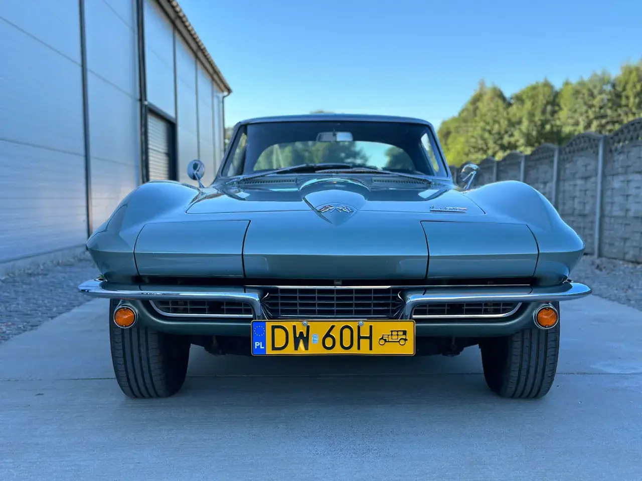 Klasyczny zielony Corvette C2 z lat 60. stoi przed nowoczesnym budynkiem.