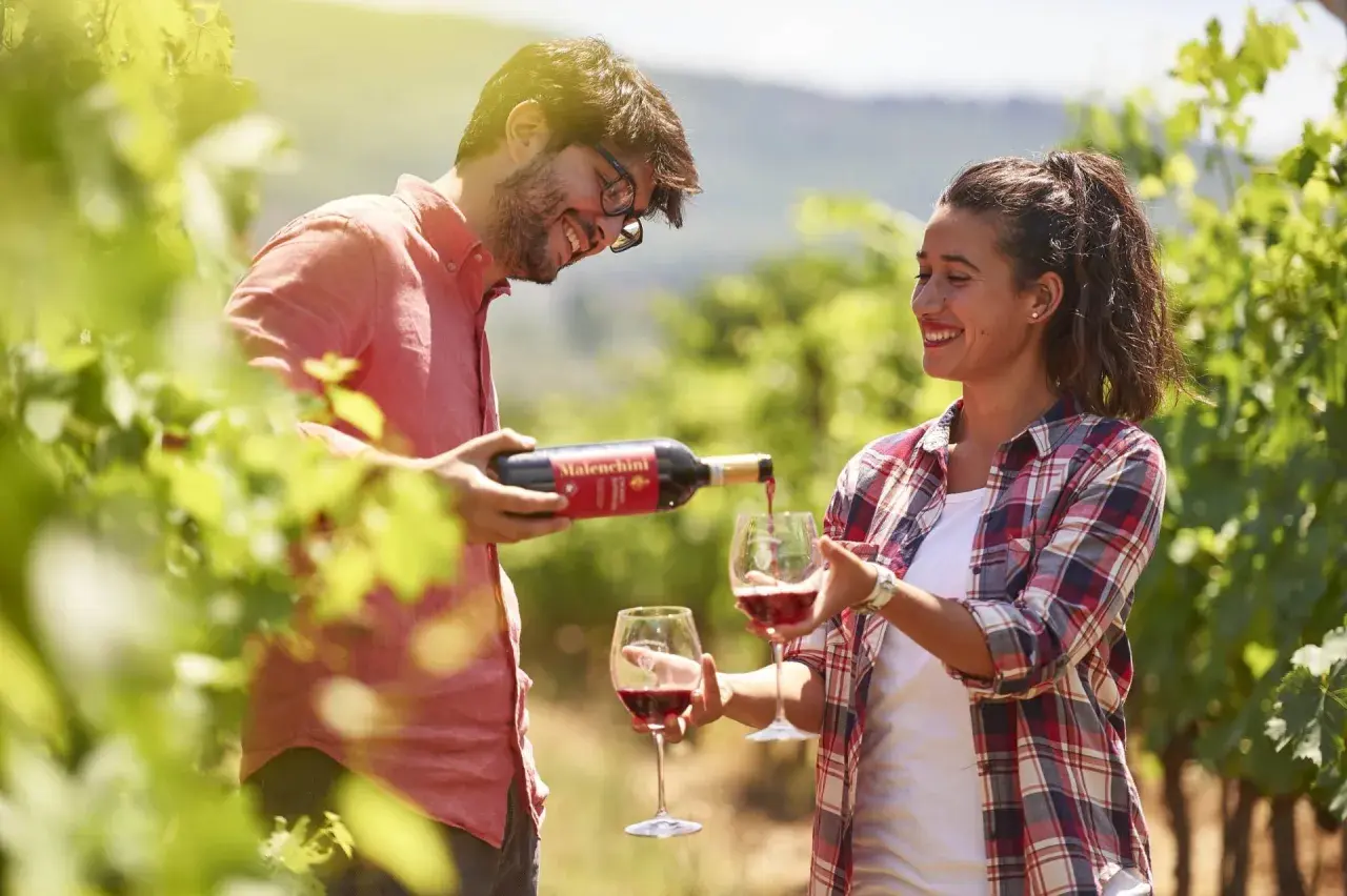 Coppia sorridente assapora il vino rosso Malenchini in un vigneto soleggiato.