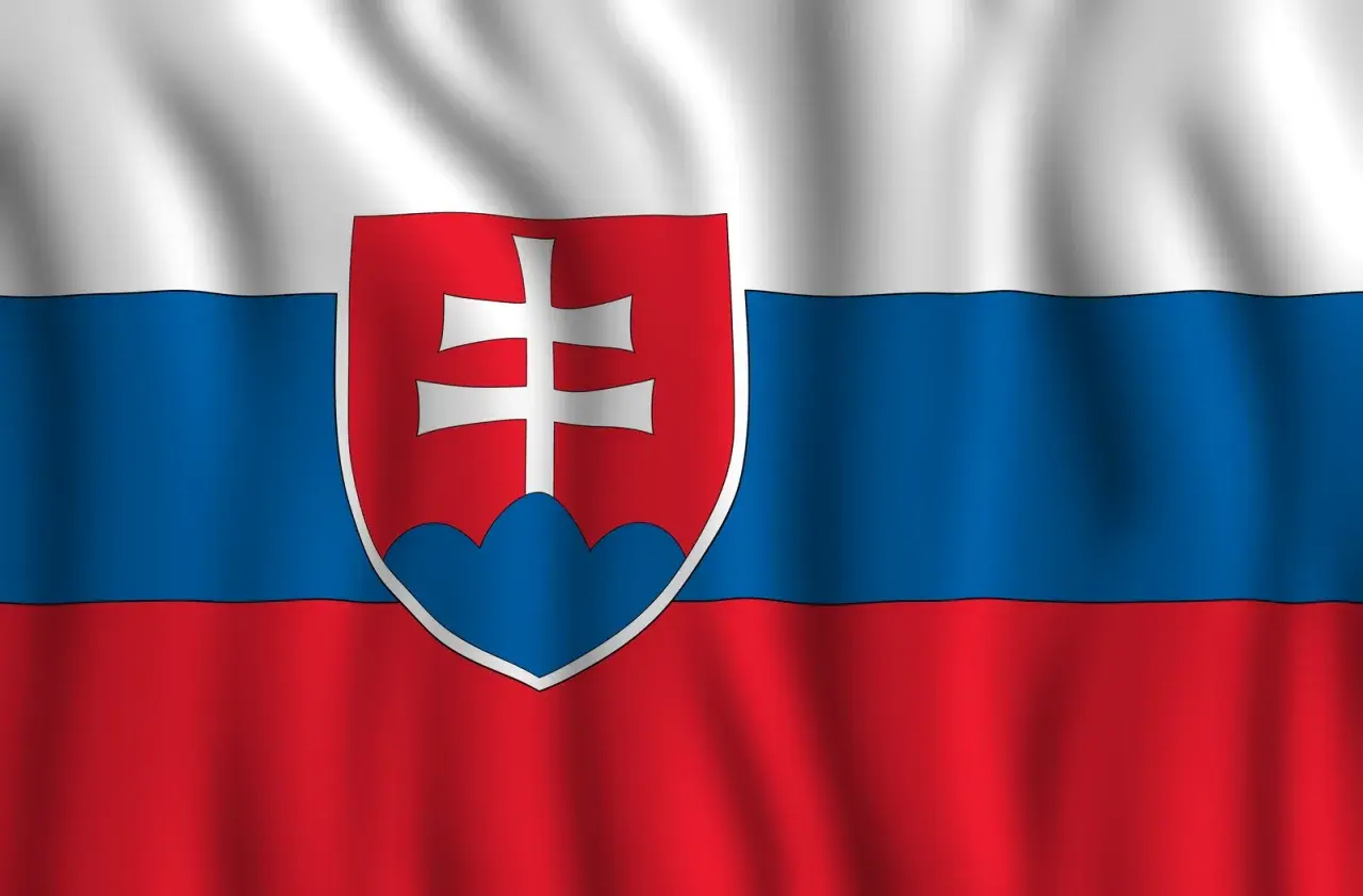 Flaga Słowacji powiewa na wietrze. Biało-niebiesko-czerwone pasy z godłem Słowacji, przedstawiającym podwójny krzyż na trzech wzgórzach.