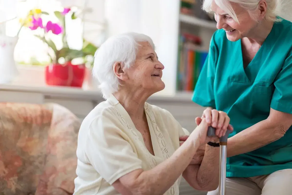 Une aide-soignante soutient une résidente souriante. Une maison de retraite moins cher offre un cadre de vie agréable et sécurisé.
