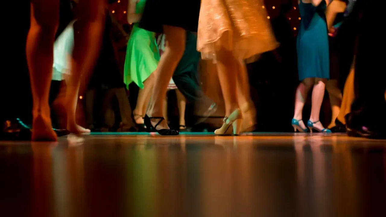 Nogi w ruchu, błyszczące sukienki i eleganckie buty. Wszyscy tańczą, tworząc dynamiczny obraz, jakby to był belgijka taniec.