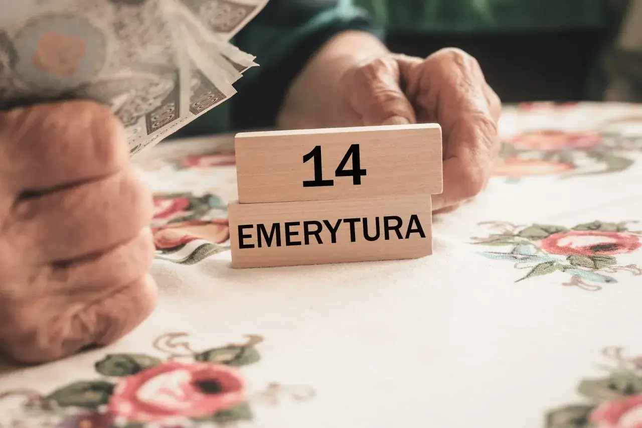 Dłonie seniora trzymają pieniądze. Na drewnianych klockach napis "14 EMERYTURA". Czekamy na 14 emeryturę 2025 netto.
