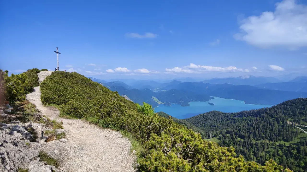 Gipfelkreuz nach einer Heimgarten Wanderung mit Blick auf einen türkisfarbenen See und Berge.