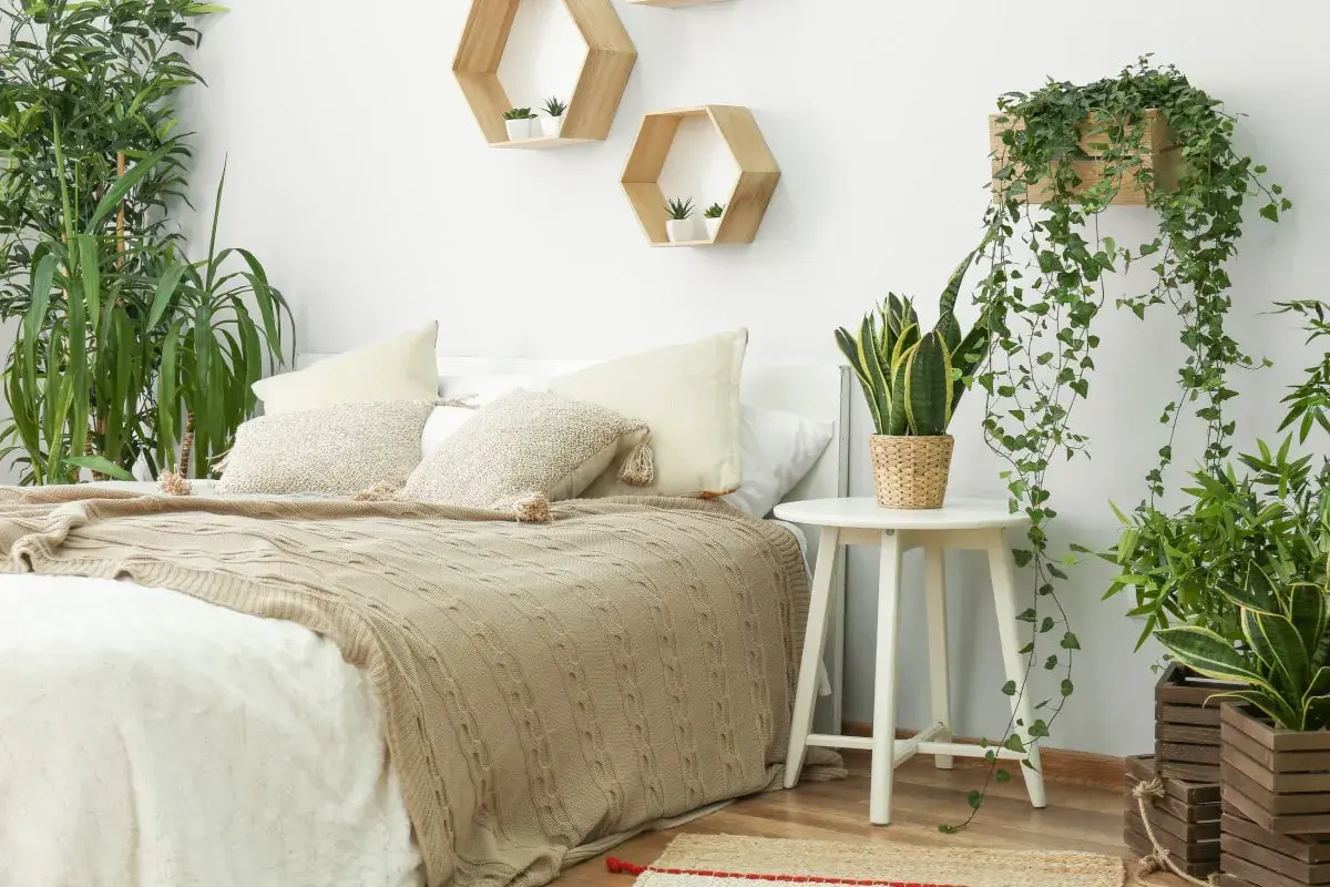Gemütliches Schlafzimmer mit vielen grünen Pflanzen. Hängende Efeutriebe und eine Bogenhanfpflanze auf einem Beistelltisch schaffen eine entspannte Atmosphäre.