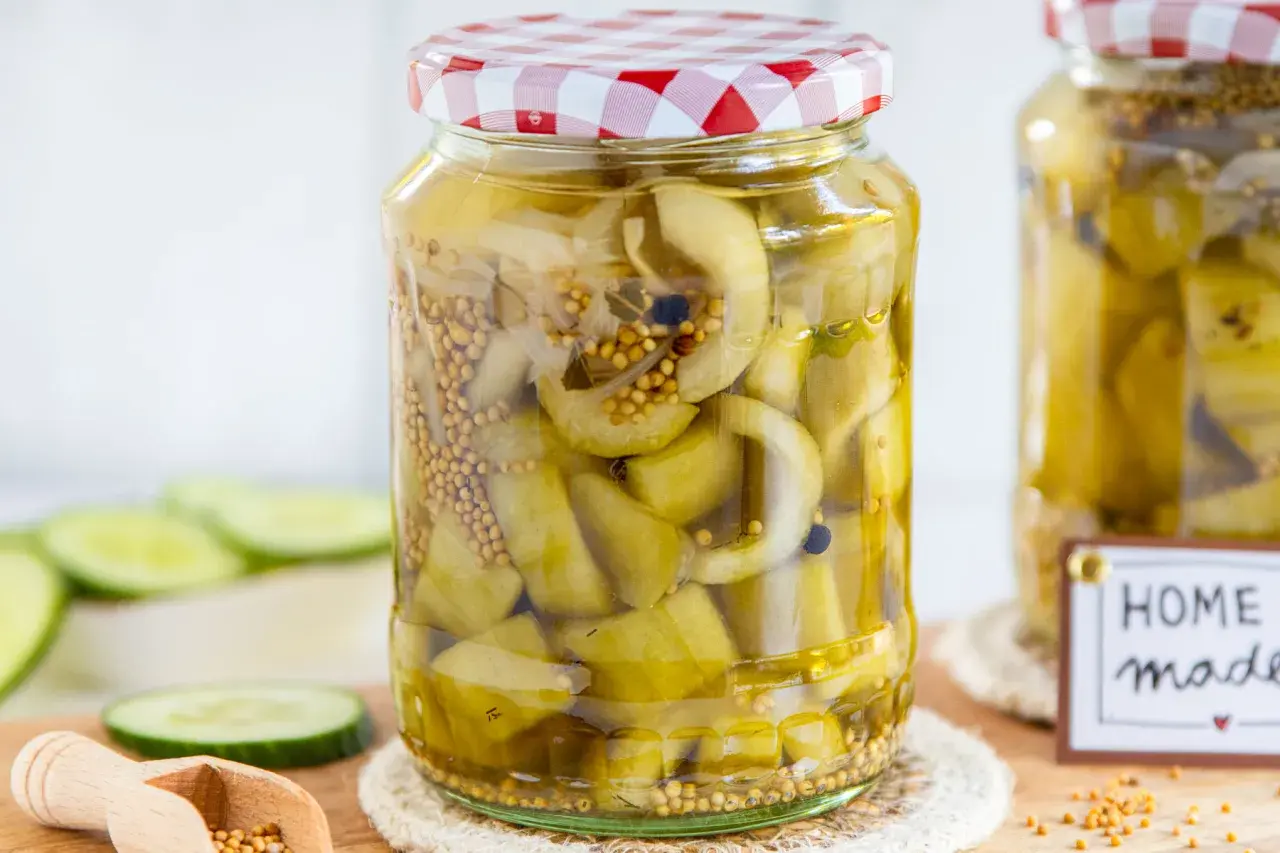 Glas mit eingelegten Senfgurken, perfekt für ein Senfgurken Rezept. Frische Gurkenscheiben und Senfkörner sind sichtbar.