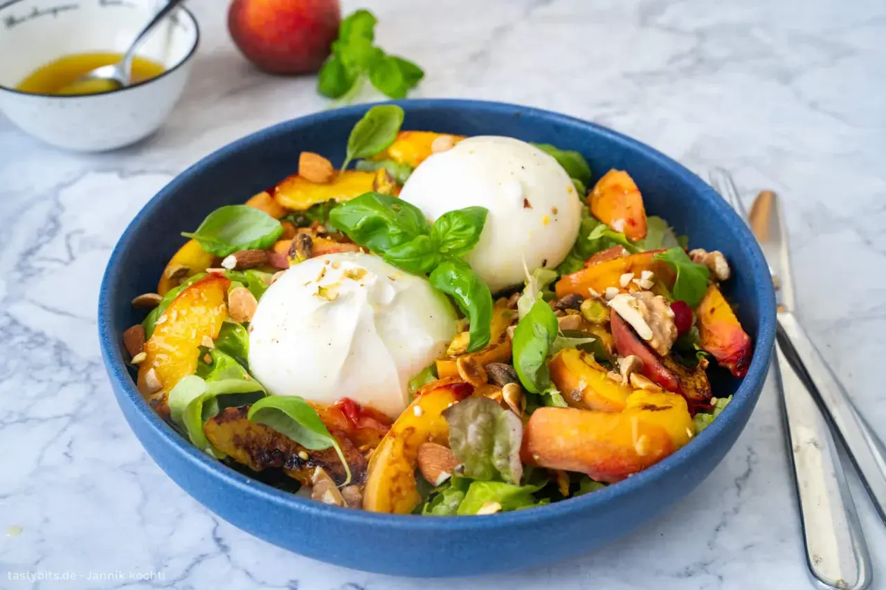 Pfirsich-Burrata-Salat mit Nüssen und Basilikum in blauer Schüssel.